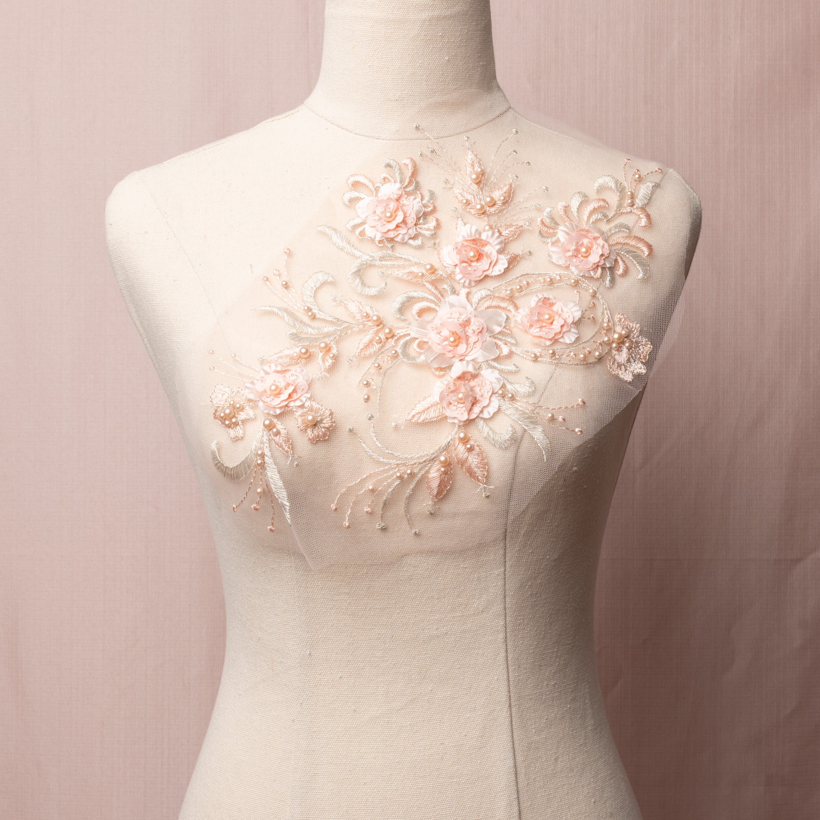 Apricot 3D floral applique embroidered onto a net backing. The flower centres and leaves are embellished with pale apricot pearls. The applique is displayed on a mannequin.