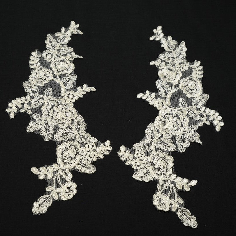 Cream embroidered applique pair laying flat on a white background.  The appliques are edged with cream cord.