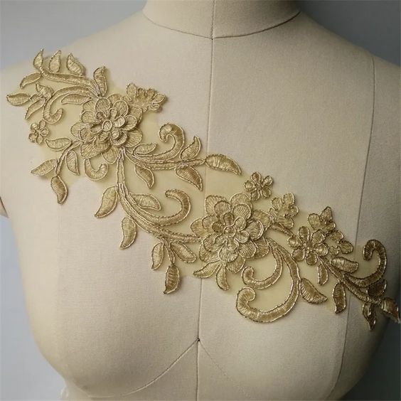 A single gold corded applique in a trailing floral design embroidered onto organza with a 3D flower near each end . Displayed across the bodice on a mannequin.