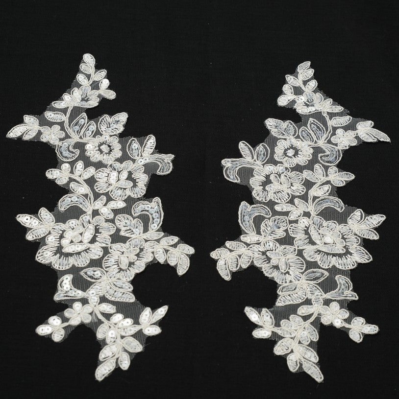 Mirrored pair of heavily embroidered white floral appliques embellished with clear sequins laying flat on a black background.