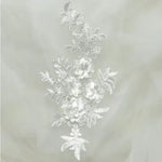 A soft white embroidered applique wiith  four 3D flowers attached to a diamond shaped spray of embroidered leaves ..