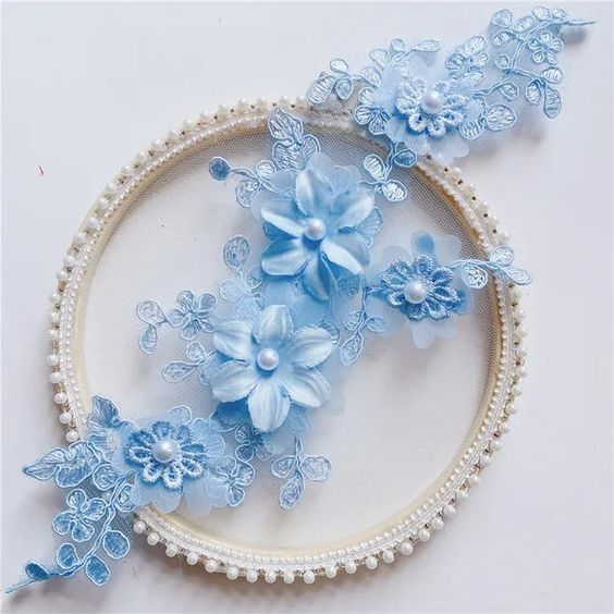 Blue embroidered applique with corded flowers and leaves. Small lace daisies are layered onto three organza 3D flowers . A single pearl decorates each flower centre. 