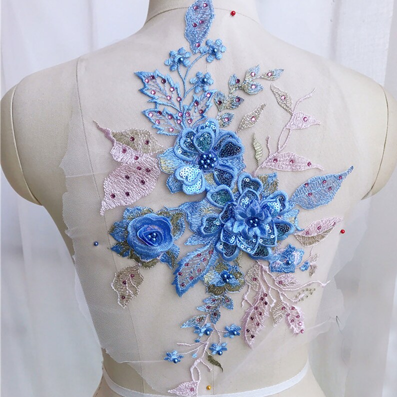 A large  3D Floral applique with 3 large blue flowers with blue sequinned petals and blue pearrl pearl centres. Pink , blue and yellow gold leaves enhance the flower spray. blue gems are sprinkled onto the leaves.embroidered leaves 