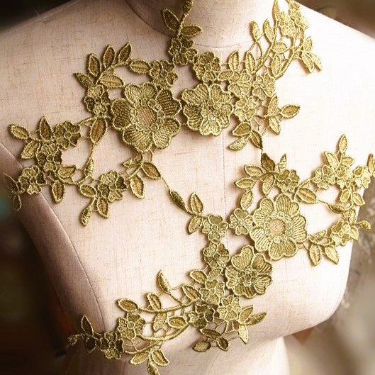 A mirrored pair of old gold embroidered venise lace appliques displayed across the bodice of a mannequin.