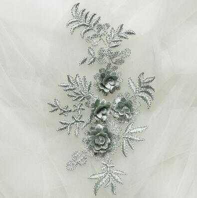 An embroidered grey applique with grey 3D embroidered flowers. Shown against a net background .