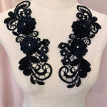 A black applique with 2 large 3d flowers  and 4 small flowers with crystal centres sewn onto an embroidered background with a swirling lattice pattern   