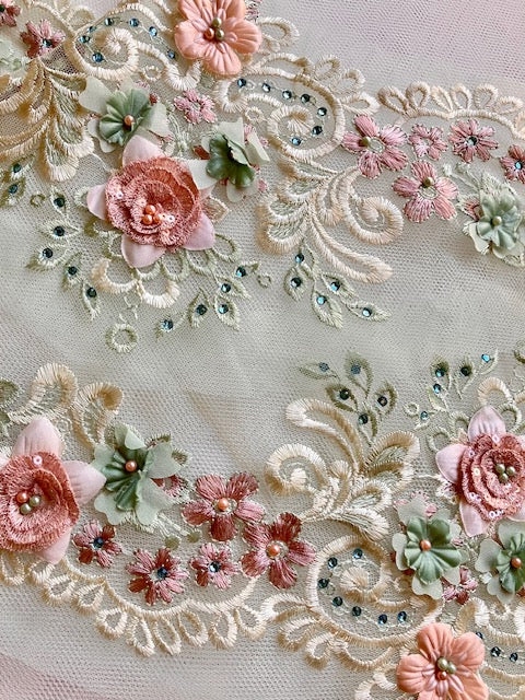 Two pieces of a 3D multi coloured dusty pink and green floral border lace displayed with the top edges of the border facing each other . 