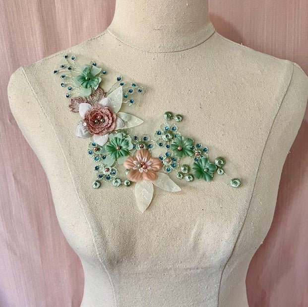 A small floral applique with sage green and dusty pink flowers ,blue gems and pearls. displayed  on a mannequin