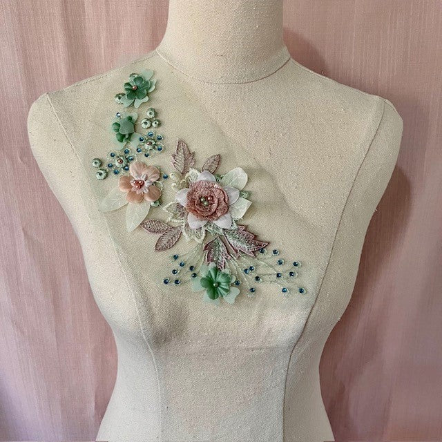 Bodice applique with a central  sequinned multilayer pink flower, three  sage green flowers with pearl centres and blue gems. 