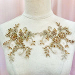  A pair of gold sequinned beaded appliques shown on a model. The  intricate floral design has with shimmering gold sequins and delicate beadwork sewn onto a fine mesh backing. The raised embroidery creates a textured surface, with clusters of tiny beads forming the centres of flowers and swirling patterns extending outward.