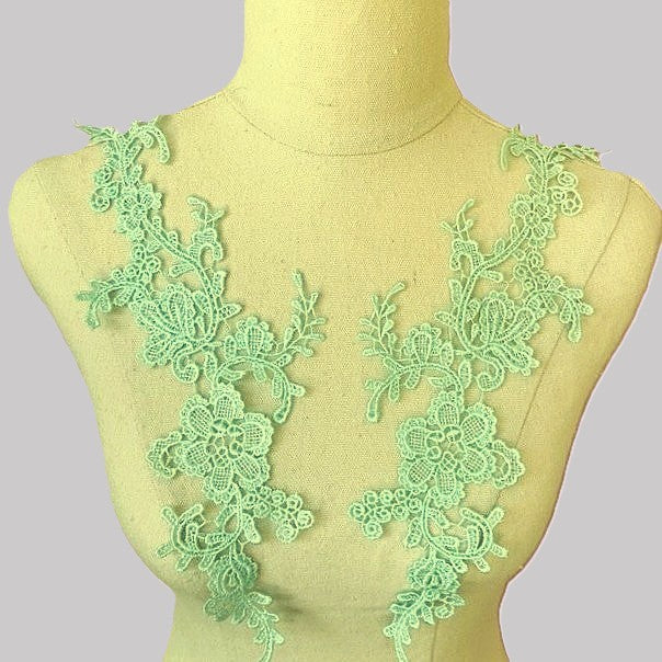 A pair of ice green floral embroidered appliques displayed on the bodice of a mannequin.  