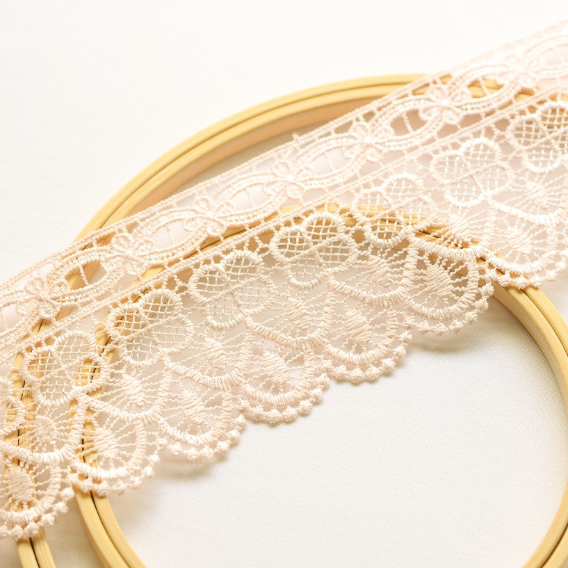 Embroidered pale pink 9 cm wide lace displayed across wooden embroidery rings.