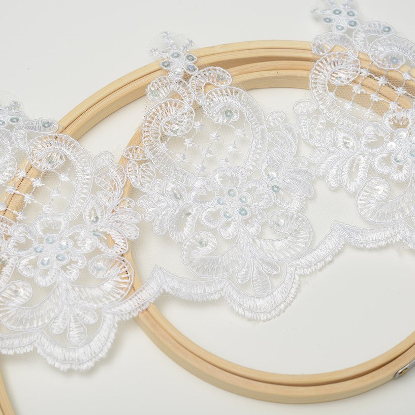 White corded and sequinned Alencon lace in a vintage medallion pattern laying diagonally across wooden embroidery rings.