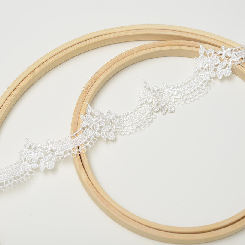 Ivory scalloped lace trim laying diagonally across wooden embroidery rings.