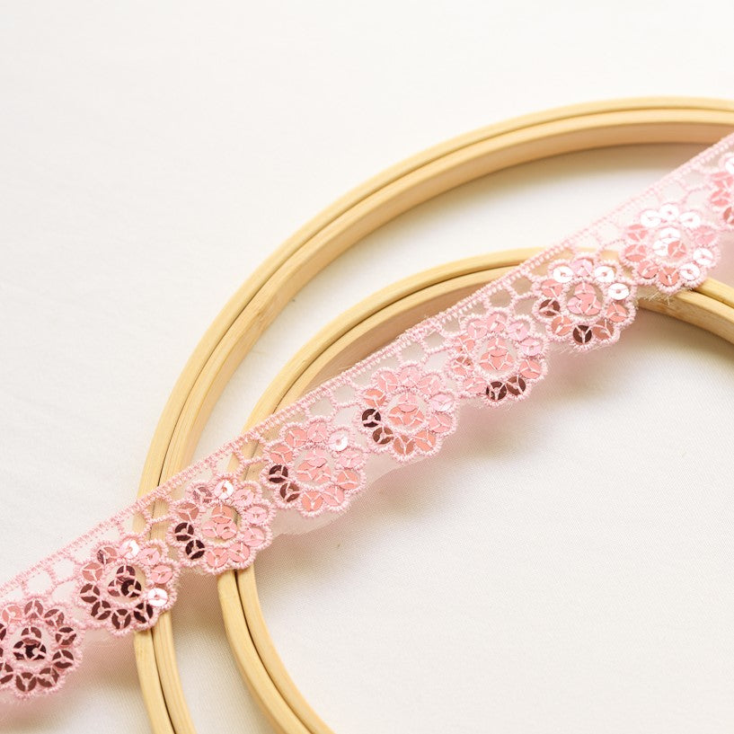 Pink daisy flower sequinned trim laying flat across wooden embroidery rings.