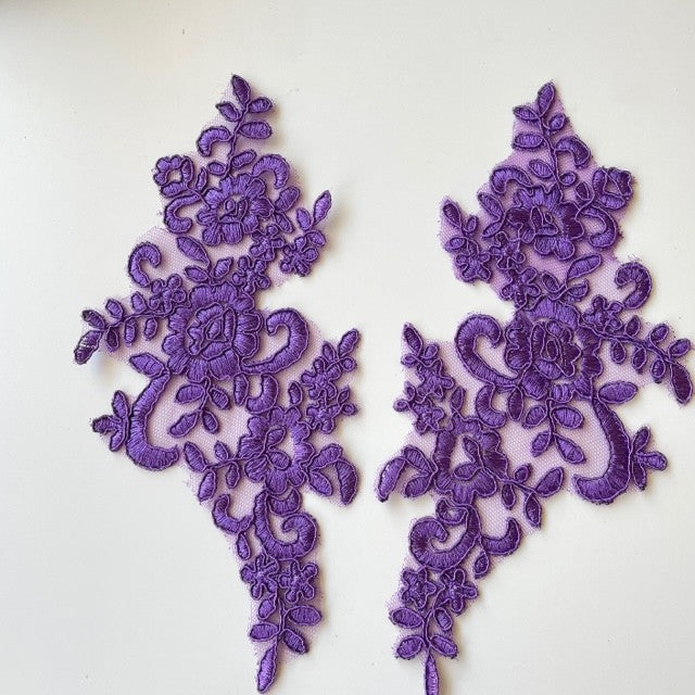 Heavily embroidered and corded purple mirrored lace applique pair.  The appliques are laying flat on a white background.