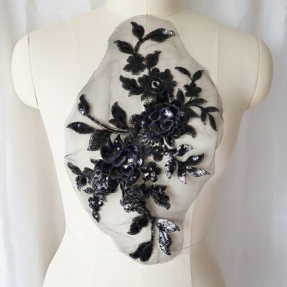 A large black sequinned applique in a floral design  embellished  with 3D flowers  with sequinned petals. The costume applique  is displayed on a mannequin.