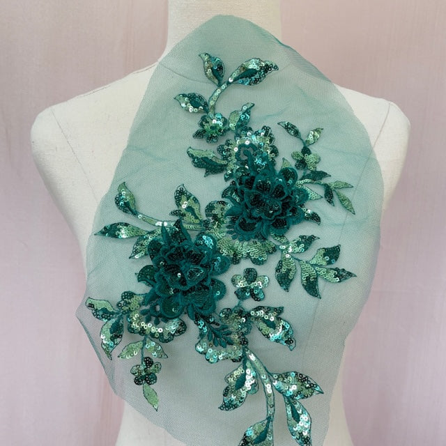 A large green sequinned applique in a floral design  embellished  with 3D flowers  with sequinned petals. The costume applique  is displayed on a mannequin.