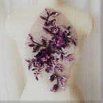 A large sequinned 3-D floral applique with purple and pinksequinned leaves stems and flowers highlighted with dusty pink sequins. Displayed on a mannequinin 