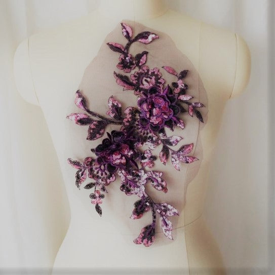 A large sequinned 3-D floral applique with purple sequinned leaves stems and flowers highlighted with dusty pink sequins. Displayed on a mannequinin 