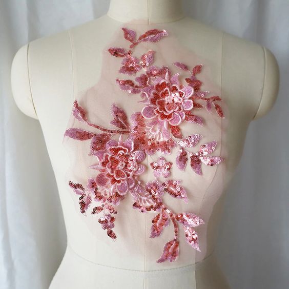 A large pink sequinned applique in a floral design  embellished  with 3D flowers  with sequinned petals. The costume applique  is displayed on a mannequin.