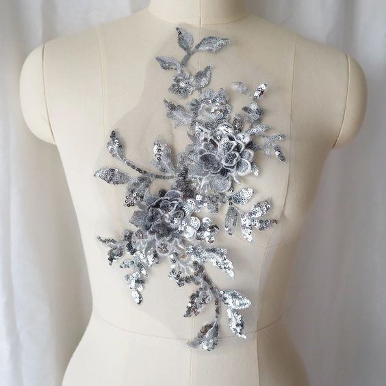 A large silver sequinned applique in a floral design  embellished  with 3D flowers  with sequinned petals. The costume applique  is displayed on a mannequin.