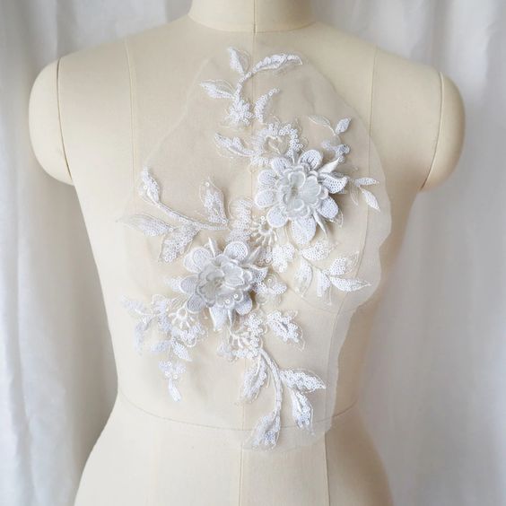 A large white sequinned applique in a floral design  embellished  with 3D flowers  with sequinned petals. The costume applique  is displayed on a mannequin.