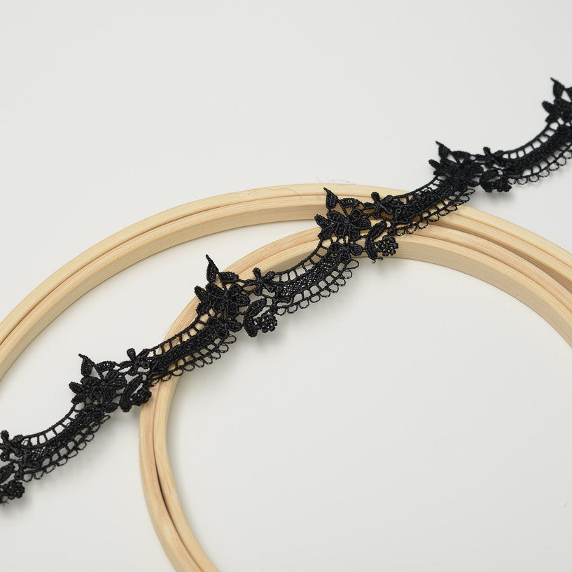 Black scalloped lace trim laying  diagonally across wooden embroidery rings.