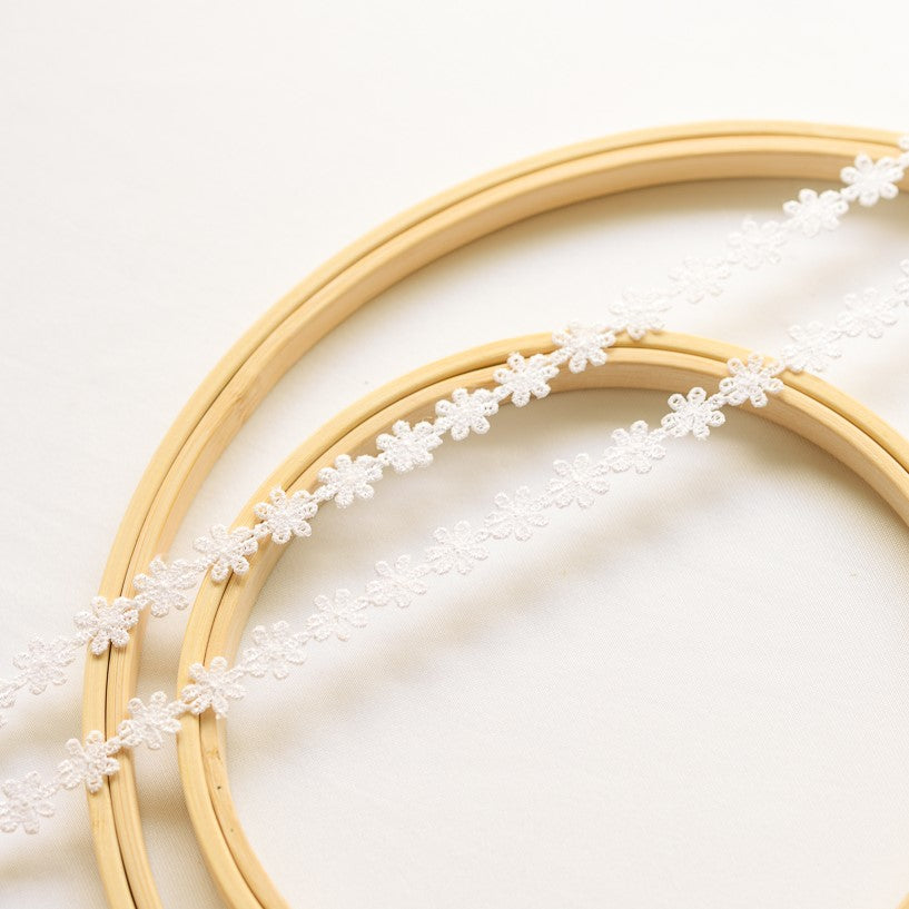 A  double strand of  small white embroidered daisy flowers laying flat across wooden embroidery rings.
