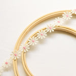 White daisy lace with pink centre draped across wooden embroidery ring.