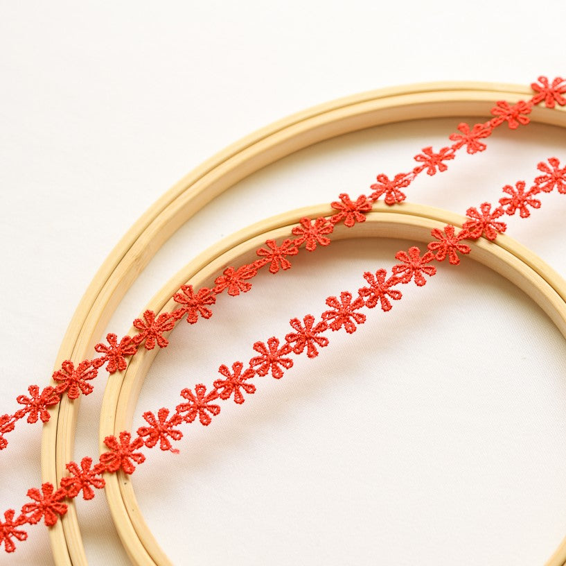 Two strands of delicate red daisy lace laying flat across wooden embroidery frames on a white background.