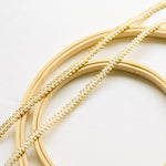 Two strands of  gimp trim with a white corded centre in a serpentine pattern. This is combined with a  metallic gold cord which outlines the looped edges on both sides of the braided trim.