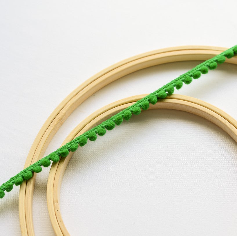 Bright green mini pom pom trim laying flat across wooden embroidery rings.