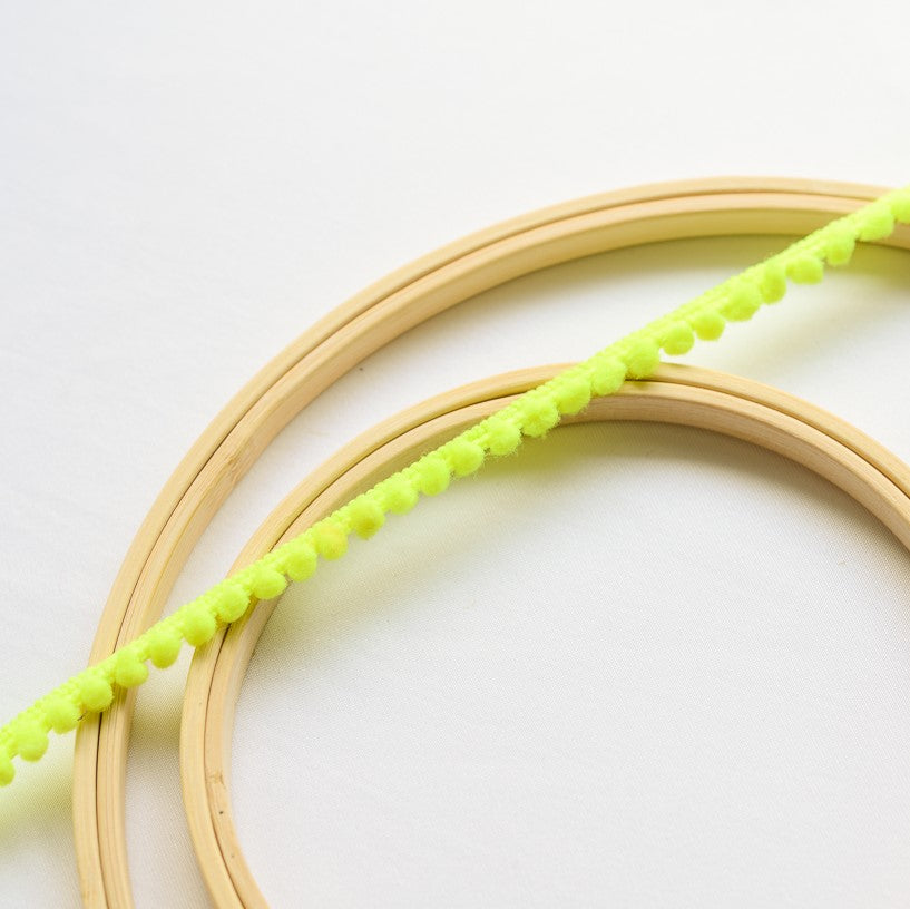 A flourescent yellow mini pom pom trim displayed across wooden embroidery rings.