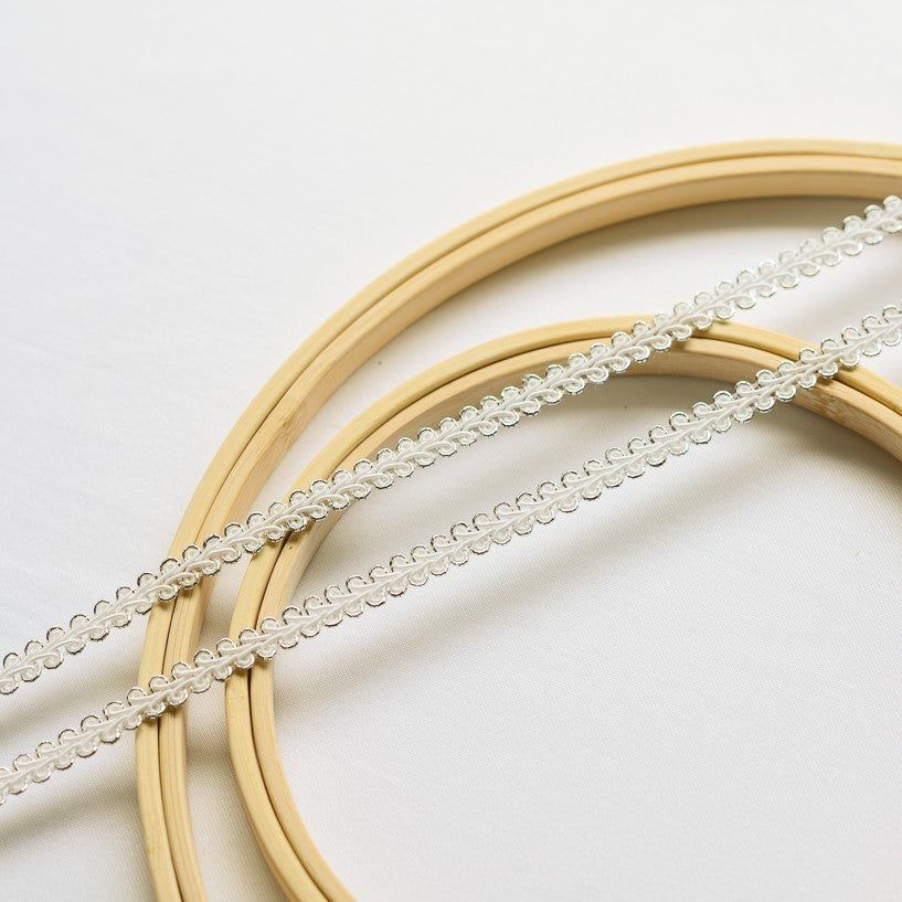 Two strands of  gimp trim with a white corded centre in a serpentine pattern. This is combined with a  metallic silvercord which outlines the looped edges on both sides of the braided trim.