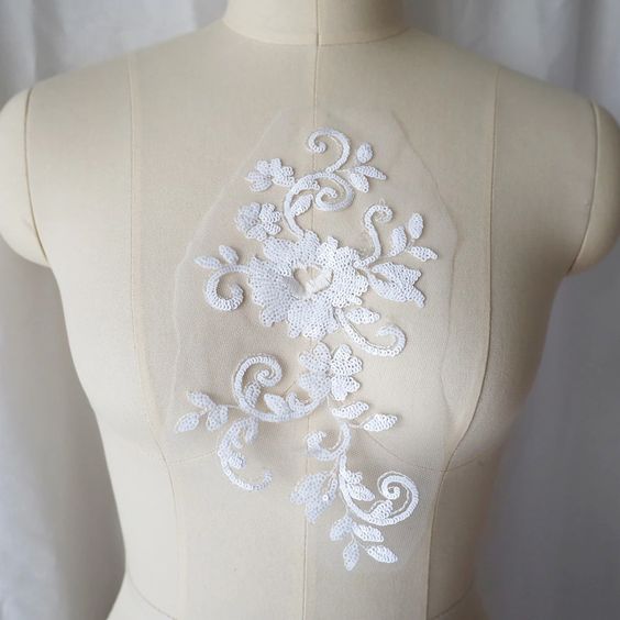 White fully sequined floral applique embroidered onto fine white net and displayed on a mannequin.