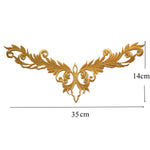 A gold v shaped applique with baroque style swirls  and  height and width measurements. 