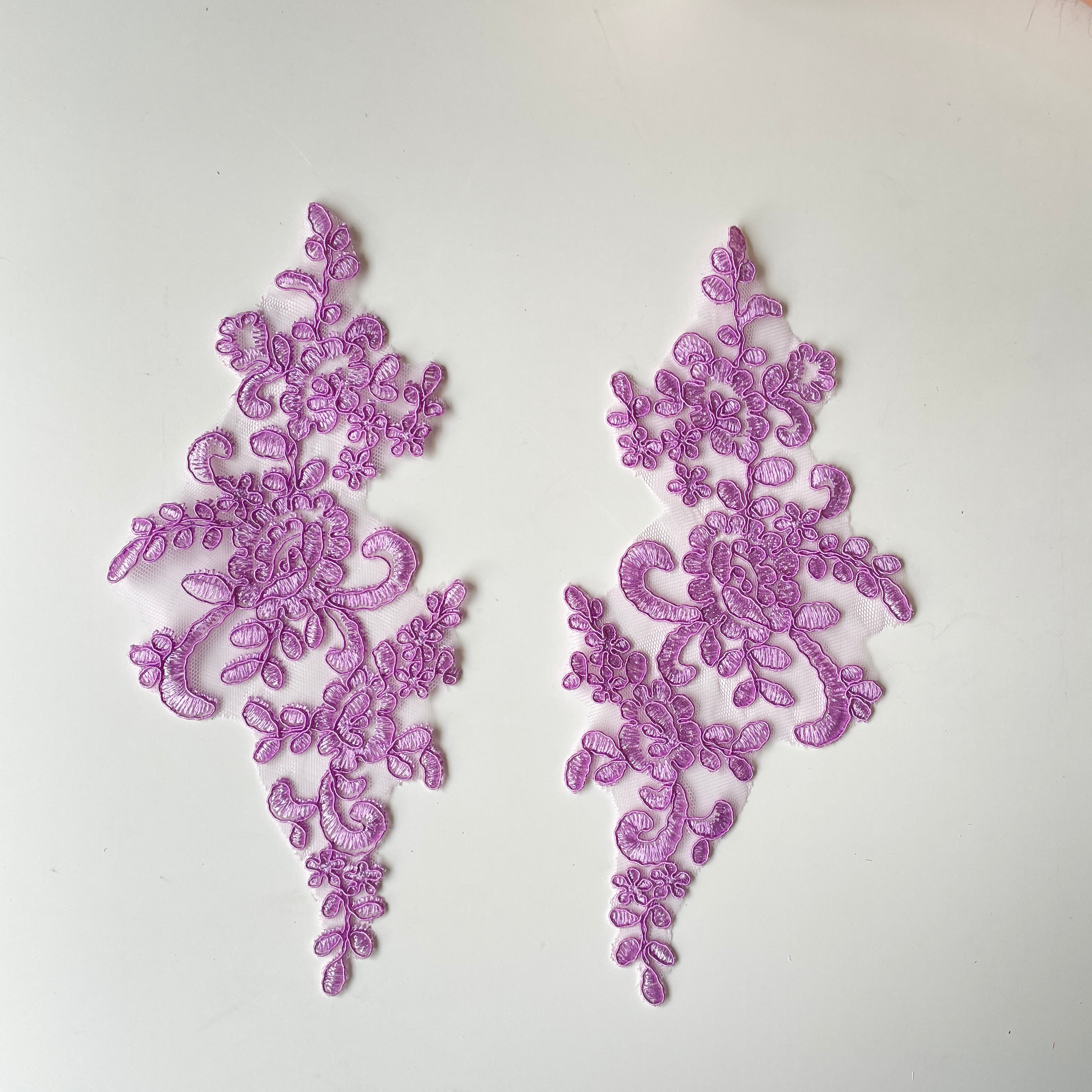 Heavily embroidered and corded purple mirrored lace applique pair. The appliques have a pink purple colour tone and are laying flat on a white background.
