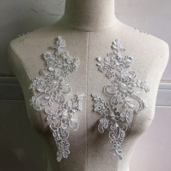 A mirrored pair of white floral sequinned appliques displayed on a mannequin .