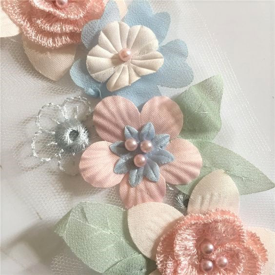 Close up view of pink, blue and green 3D floral applique on a white background.