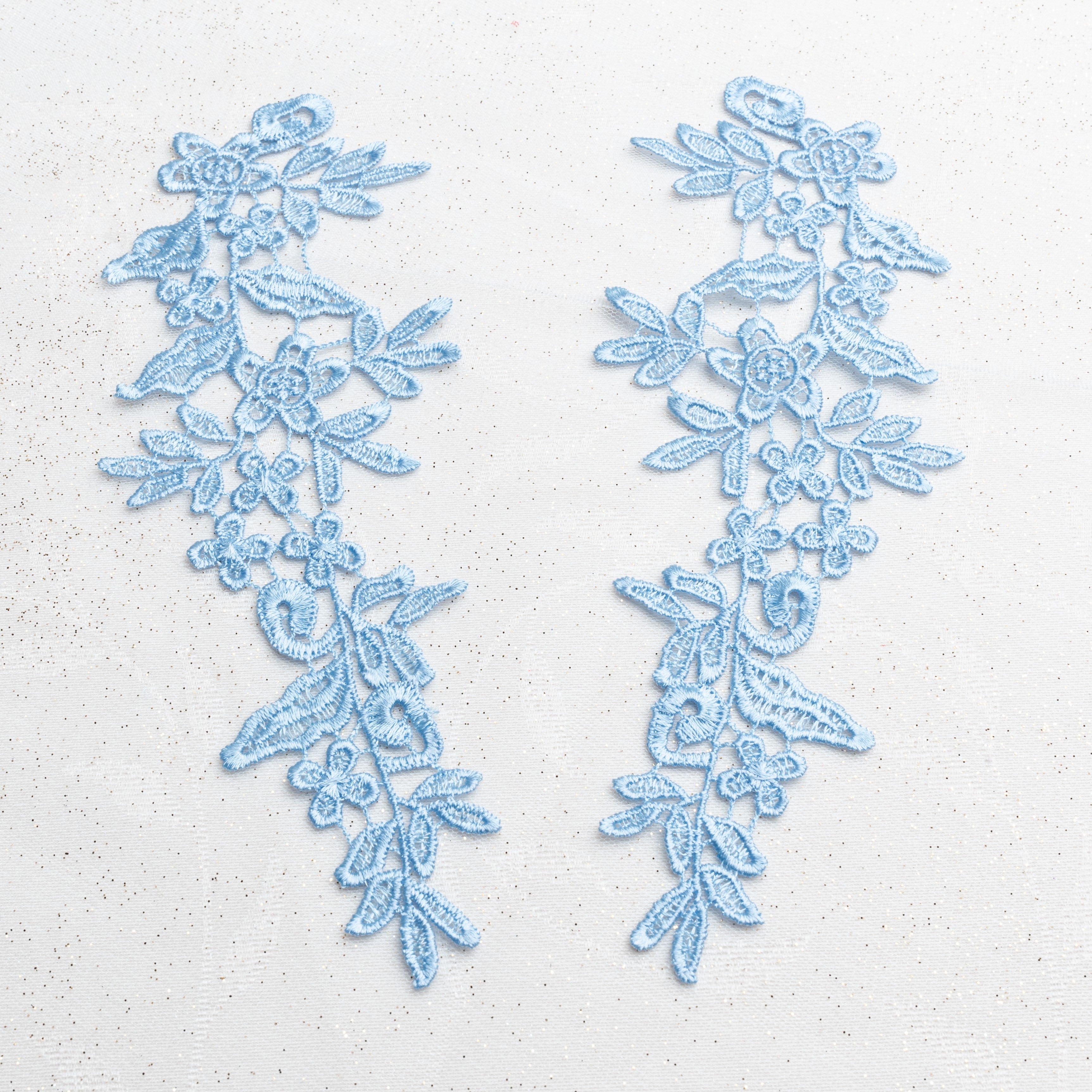 Heavily embroidered sky blue mirrored lace applique pair laying flat on a white background.