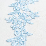 Close up of heavily embroidered sky blue floral applique on a white background.