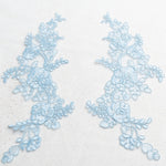 Pale blue embroidered applique pair laying flat on a white background.  The appliques are edged with pale blue cord.