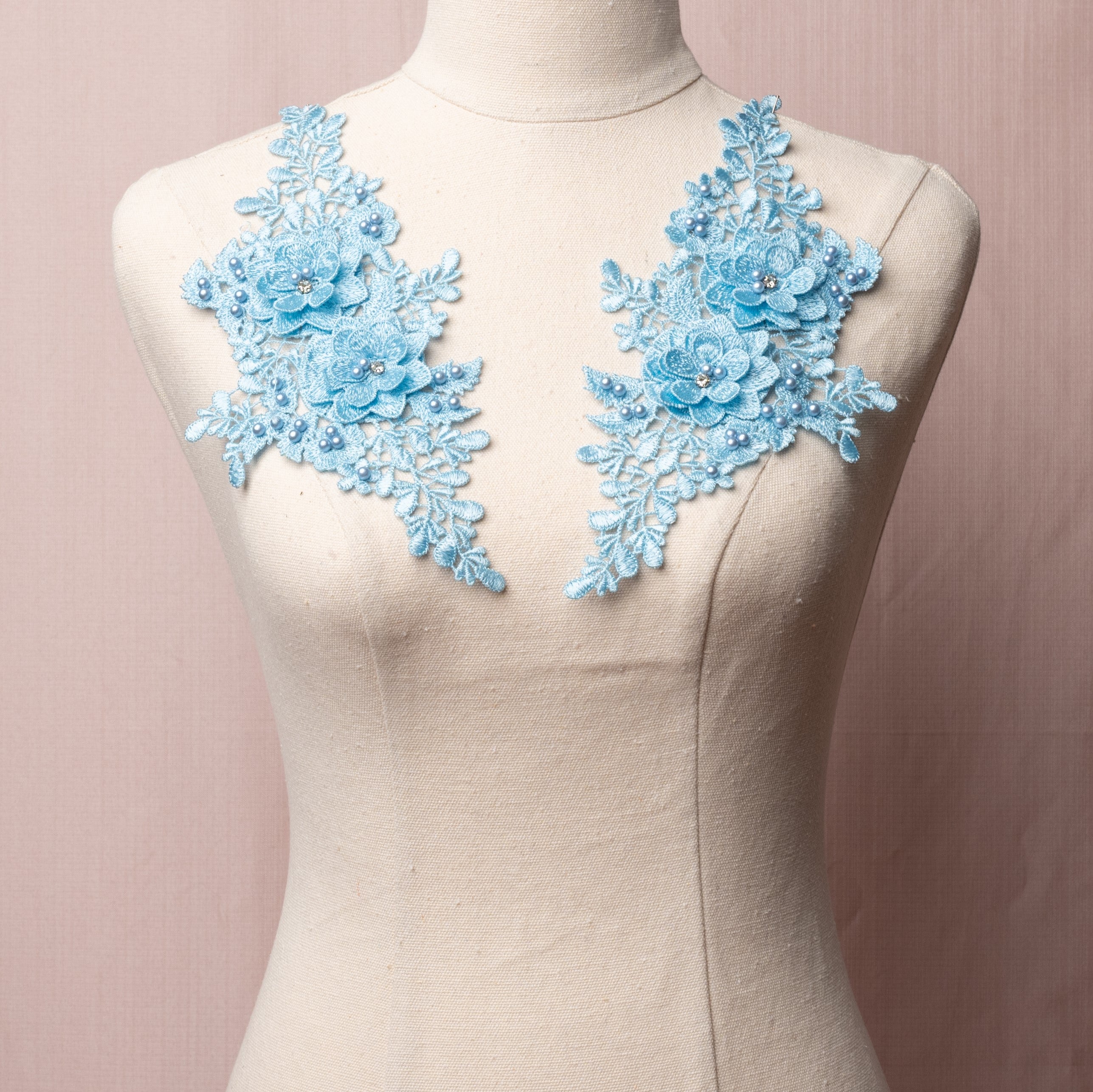 Pale blue embroidered applique pair with 3D flowers.  The applique is embellished with a scattering of blue pearls and the 3D flowers have a crystal centre and are displayed on a mannequin.