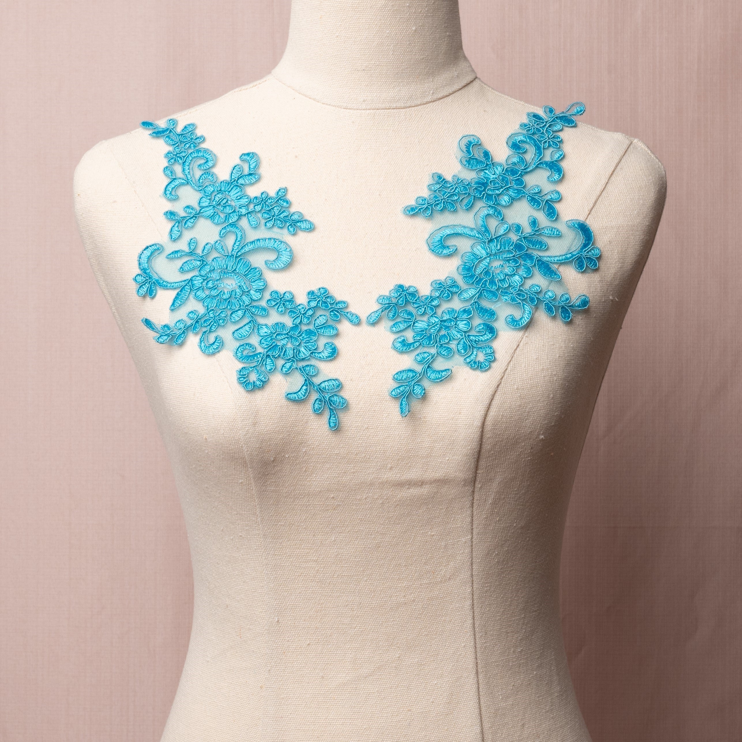 Lake blue floral corded applique pair embroidered onto a fine net backing.  The appliques are displayed on a mannequin.