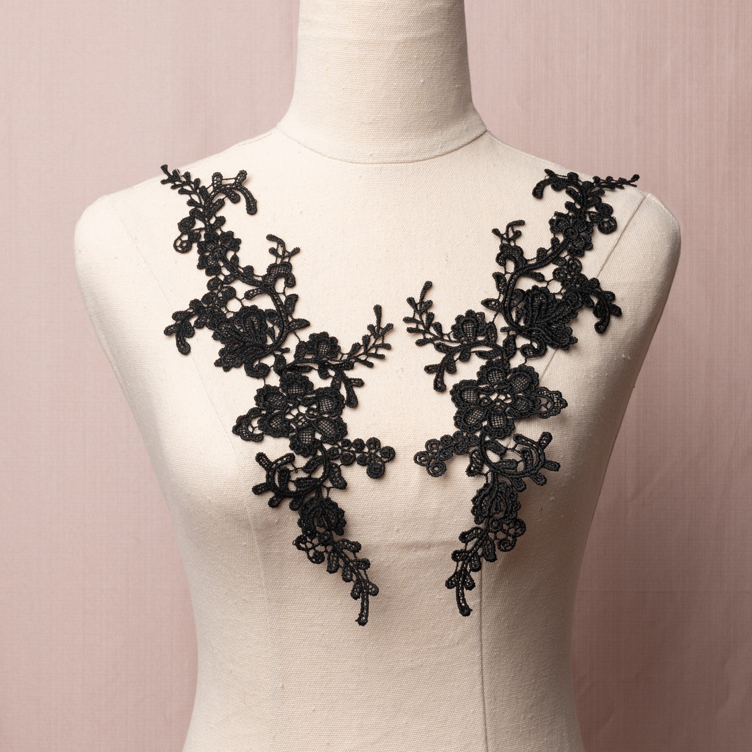 A black floral  embroidered costume applique pair displayed on a mannequin .