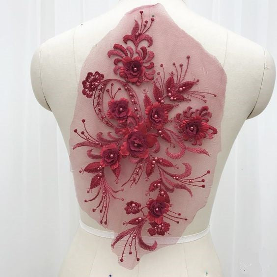 Burgundy red floral 3D applique piece embroidered onto a net backing and embellished wit burgundy pearl beads.  The applique is displayed on a mannequin. 