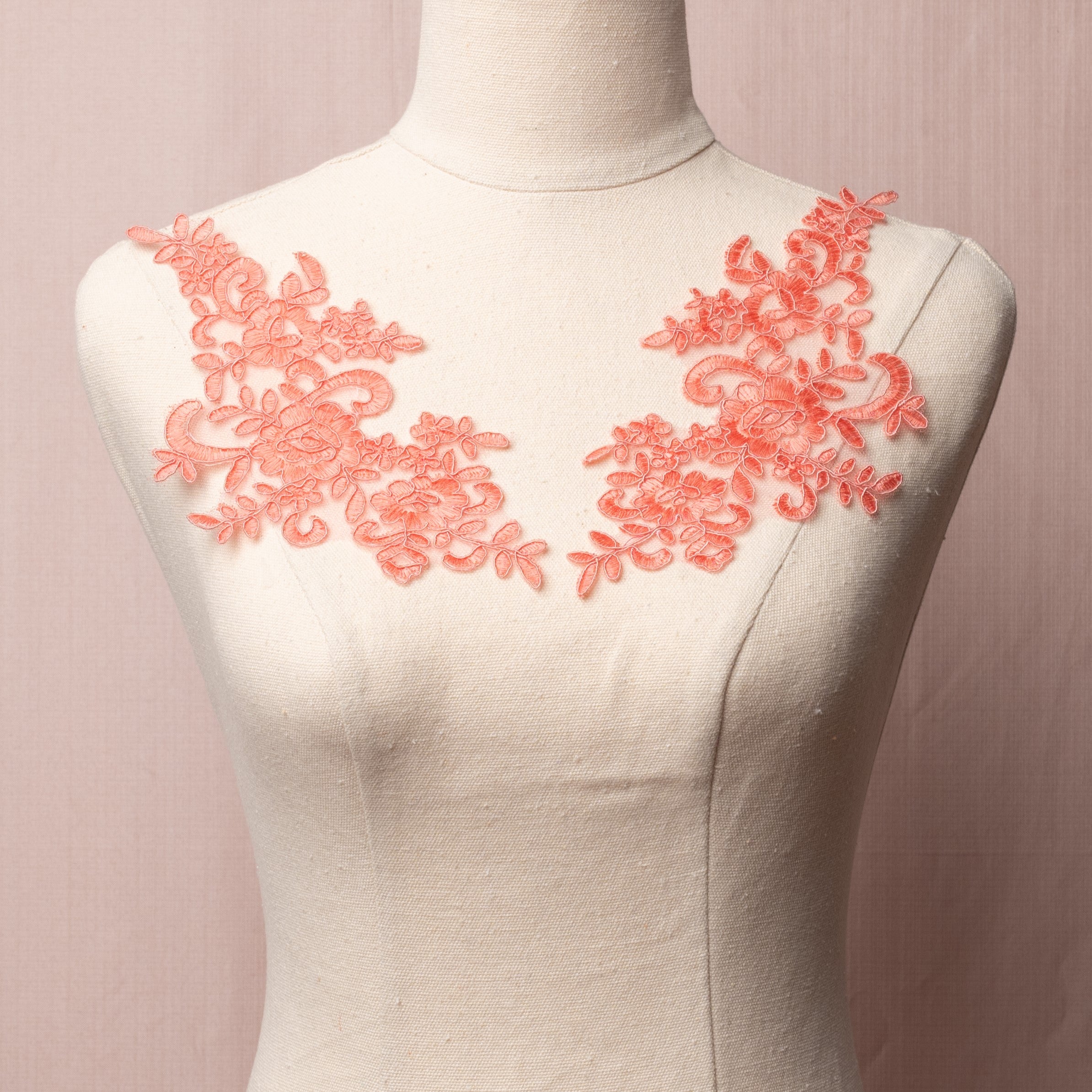 Coral pink floral corded applique pair embroidered onto a fine net backing.  The applique pair is displayed on a mannequin.