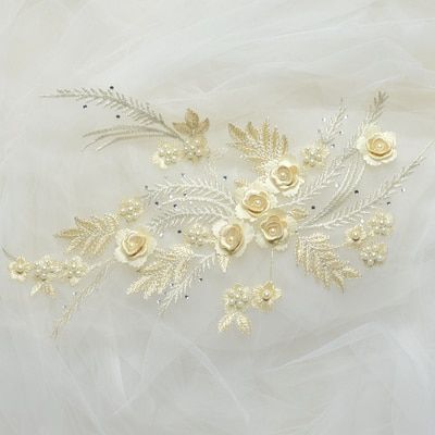 An embroidered floral spray of satin and metallic threads. The champagne costume applique features multi layered embroidered flowers with champagne pearl centres and metallic embroidered fern fronds.  The  applique is laying flat on a white background.