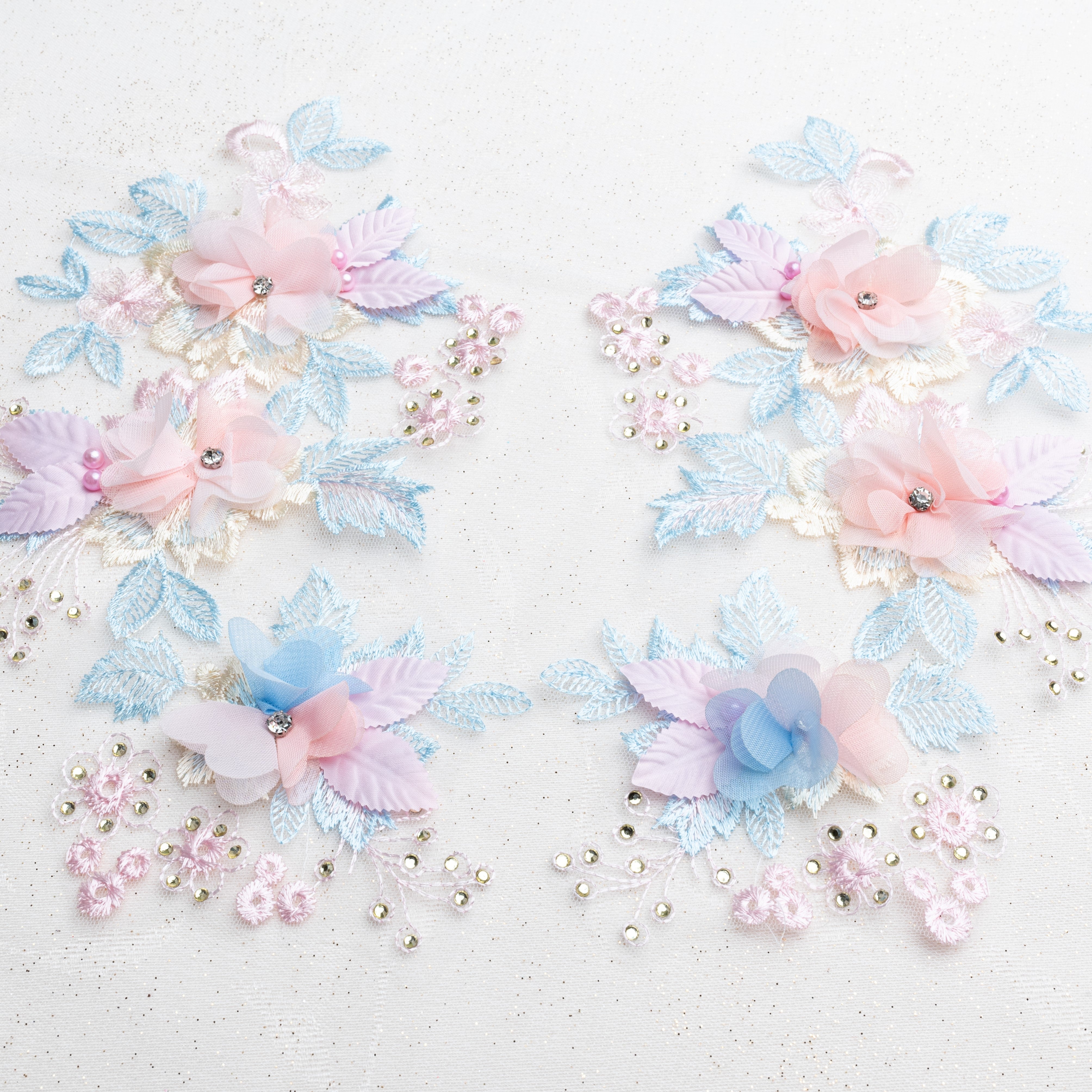 Floral applique pair with 3D blue and pink flowers laying flat on a white background.